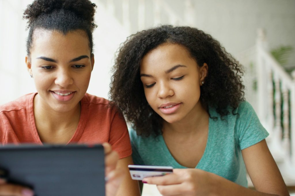 Two young women looking at a tablet with a bank card