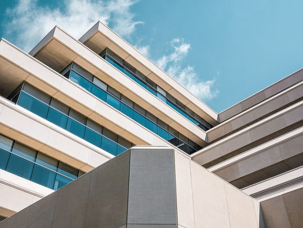 Modern office building with rows of blue glass windows photographed from below against a partly cloudy sky.