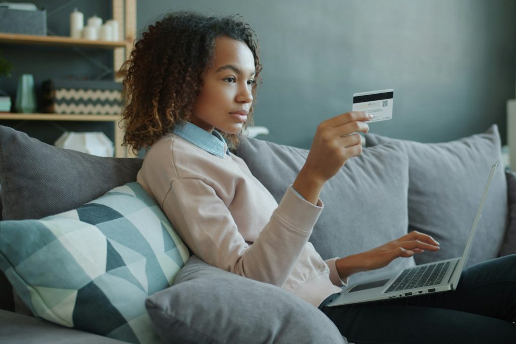 A woman on a sofa holding a credit card and a laptop