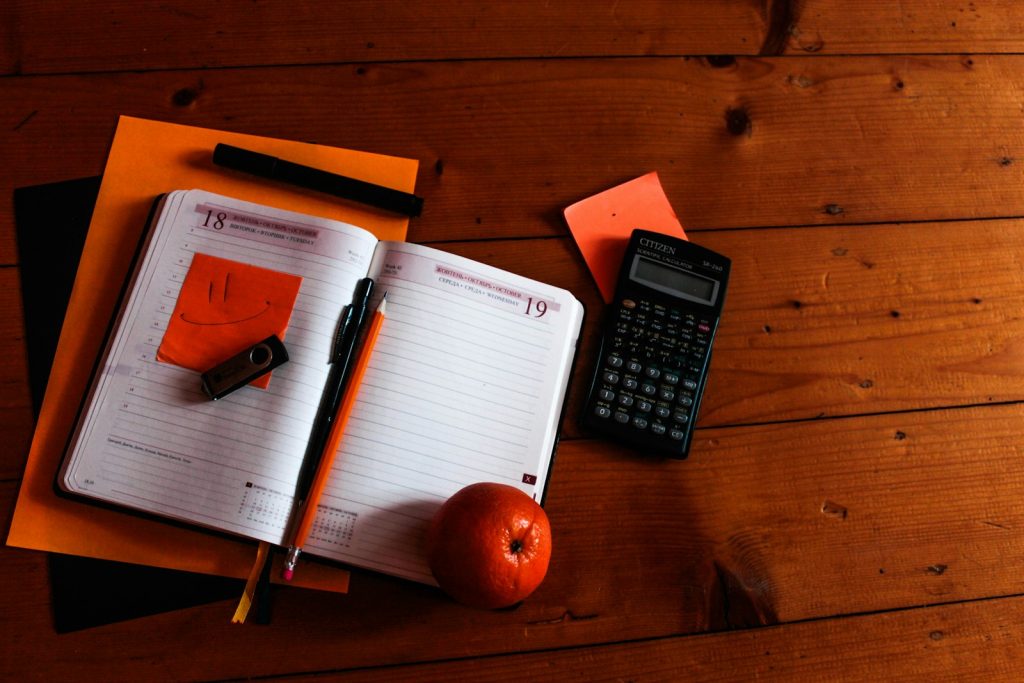 A notebook, calculator and pen on a wooden desk