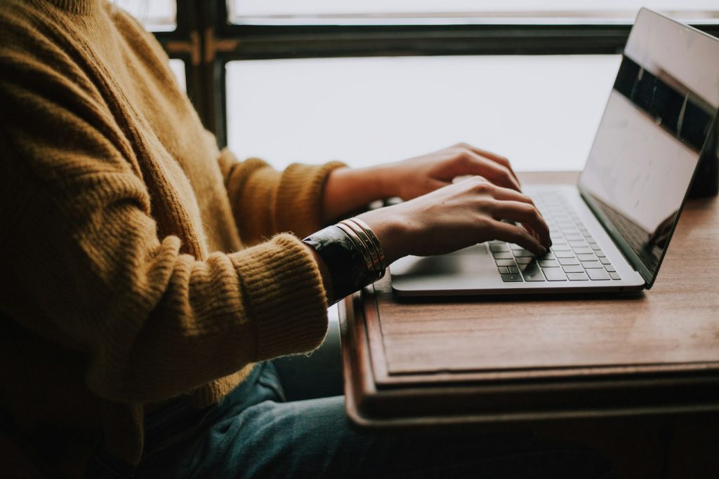 A person typing on a laptop at a wooden table